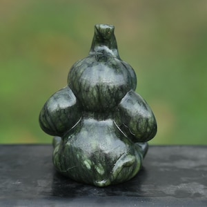 May include: A dark green, carved stone sculpture of a duck or bird. The sculpture has a smooth, polished appearance with visible veining. The bird is depicted in a seated position, with its wings folded and head upright. The background is blurred.