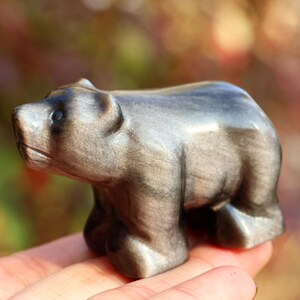 Könnte beinhalten: Kleine, geschnitzte Bärenfigur in Grau- und Schwarztönen. Der Bär steht auf allen Vieren, mit einer glatten, polierten Oberfläche. Die Figur ist ein dekorativer Gegenstand, wahrscheinlich aus Stein oder einem ähnlichen Material.