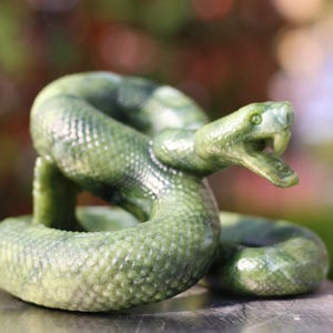Op de afbeelding: Een groene jadesculptuur van een slang die zich in een verdedigende positie oprolt met zijn bek open. De slang is gebeeldhouwd met realistische details, waaronder schubben en hoektanden.