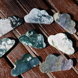 May include: A collection of seven cloud-shaped stones with unique patterns. The stones feature a mix of white, green, and blue hues, with intricate veining and marbling. They are arranged on a wooden surface, showcasing their natural beauty.