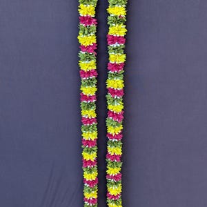 May include: Two vertical garlands composed of colorful artificial flowers. The garlands alternate sections of yellow, pink, and green flowers, with small white accents. The background is a solid dark gray.