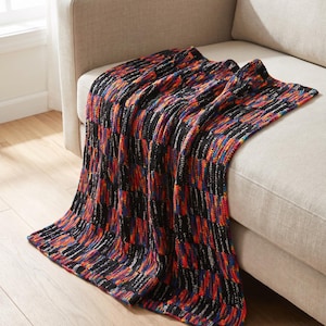 May include: A rectangular knit throw blanket featuring a repeating pattern of solid black vertical stripes alternating with textured, multi-colored stripes in vibrant shades of red, orange, blue, and yellow, draped over a neutral-colored sofa.