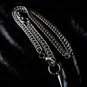 May include: A silver chain necklace with a pointed pendant. The chain is made of interlocking metal rings.