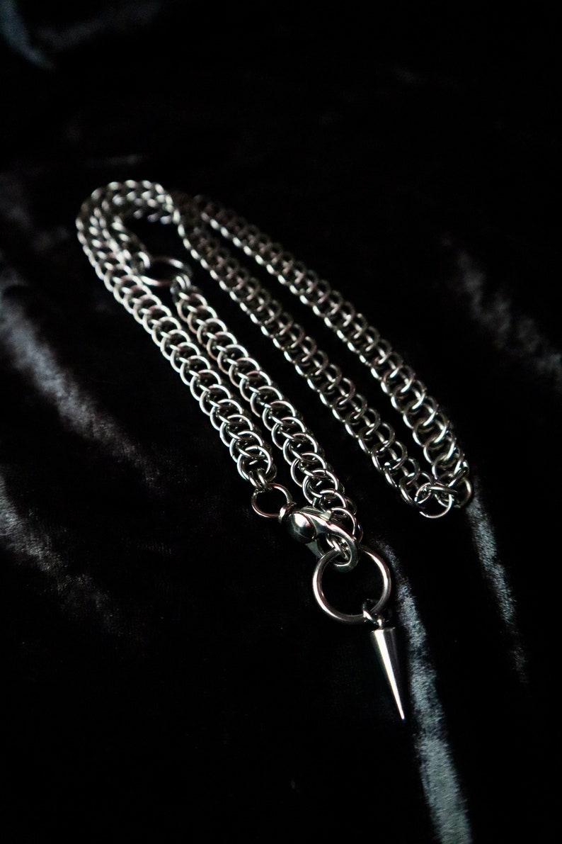 May include: A silver chain necklace with a pointed pendant. The chain is made of interlocking metal rings.