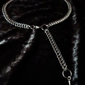 May include: A silver chain necklace with a pointed pendant. The necklace is made of multiple strands of chain and has a simple clasp.