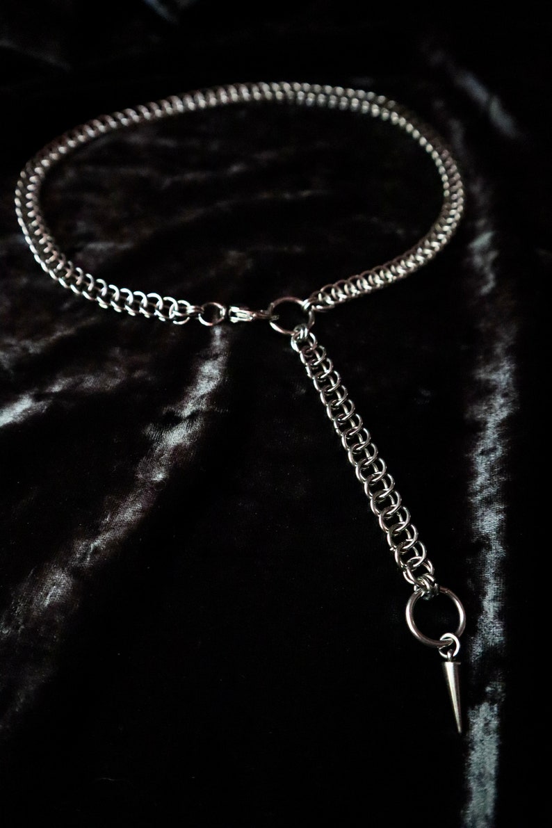 May include: A silver chain necklace with a pointed pendant. The necklace is made of multiple strands of chain and has a simple clasp.