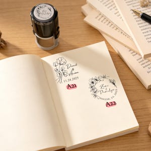 Puede incluir: Un sello autoentintable negro y plateado con un diseño floral se encuentra junto a un cuaderno abierto con diseños florales estampados y texto. Las páginas del cuaderno son de color crema y los sellos son de tinta negra. El texto incluye nombres y fechas.