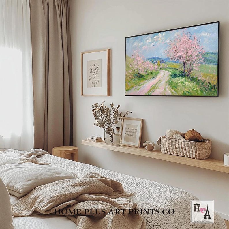 K&ouml;nnte beinhalten: Ein Schlafzimmer-Interieur mit einem wei&szlig;en Bett, einem Holzregal und einem gerahmten Gem&auml;lde einer Landschaft mit einem gewundenen Weg und rosa bl&uuml;henden B&auml;umen. Das Gem&auml;lde befindet sich &uuml;ber dem Regal, das mit einer Vase mit Trockenblumen, einem Buch und einem Weidenkorb dekoriert ist.