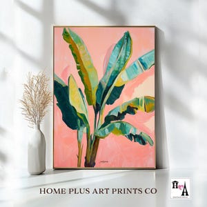 May include: A framed artwork featuring a vibrant banana leaf painting. The leaves are rendered in shades of green and yellow against a soft pink background. The artwork is signed and framed in a gold tone. The text "HOME PLUS ART PRINTS CO" is at the bottom.