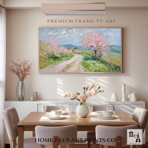 K&ouml;nnte beinhalten: Ein gerahmtes Gem&auml;lde, das eine rosa und gr&uuml;ne Landschaft mit einem gewundenen Feldweg zeigt, der zu einem kleinen Dorf f&uuml;hrt. Das Gem&auml;lde h&auml;ngt an einer wei&szlig;en Wand &uuml;ber einem Esstisch aus Holz mit St&uuml;hlen. Der Text "PREMIUM FRAME TV ART" befindet sich &uuml;ber dem Gem&auml;lde und der Text "HOME PLUS ART PRINTS CO" unter dem Gem&auml;lde.