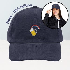 May include: Navy blue corduroy baseball cap with an embroidered beer mug and rainbow design. The text "Navy - USA Edition" is printed on the side. A woman is wearing a similar cap in a circular inset.