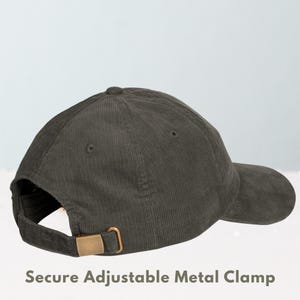 May include: A dark green corduroy baseball cap with a curved brim. The cap features a secure adjustable metal clamp in a gold color on the back for size adjustment. The text "Secure Adjustable Metal Clamp" is visible at the bottom of the image.