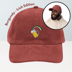 May include: Burgundy corduroy baseball cap with an embroidered beer mug and rainbow design. The text "Burgundy - Irish Edition" is printed on the side. A man wearing a similar cap is shown in a circular inset.