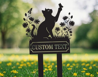 May include: Black metal cat garden stake with a butterfly and floral accents. The cat is reaching up towards a butterfly. The sign reads "CUSTOM TEXT". The stake is in a grassy area with yellow flowers.