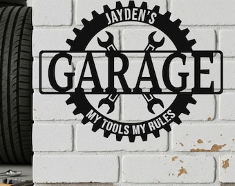 May include: Black metal garage sign with the text "JAYDEN'S GARAGE" and "MY TOOLS MY RULES". The sign features a gear design with crossed wrenches, mounted on a white brick wall.