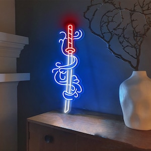 K&ouml;nnte beinhalten: Ein blaues Neon-Schild, das ein Schwert mit roten Akzenten zeigt, umgeben von stilisierten Wellen. Das Schild ist an einer Wand &uuml;ber einem Holzregal angebracht.