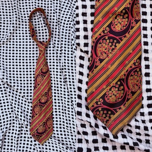 Könnte beinhalten: Eine gemusterte Krawatte mit roten, goldenen und schwarzen Streifen und Paisley-Designs. Die Krawatte wird vor einem schwarz-weiß gemusterten Hintergrund präsentiert. Ein klassisches Accessoire für formelle oder geschäftliche Kleidung.