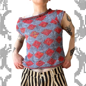 May include: A sleeveless knit top featuring a light blue base with a repeating red diamond pattern. The garment has a wide, asymmetrical neckline and a loose, textured weave. It is paired with beige and black vertically striped trousers.