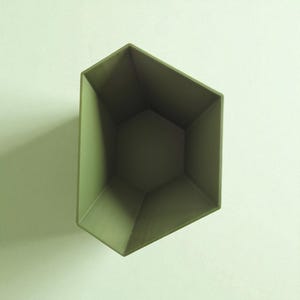 May include: An olive green, geometric-shaped container with a faceted design. The container has a hexagonal base and angled sides, creating a modern, minimalist aesthetic. The interior is a darker shade of green.