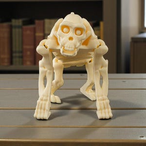 May include: A cream-colored primate skeleton figurine, posed in a quadrupedal stance. The detailed sculpture features a skull with eye sockets and a rib cage, set on a wooden surface. The background includes a bookshelf with various books.