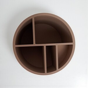 May include: A brown, circular wall shelf with five compartments. The shelf is made of a solid material and is mounted on a white wall. The compartments are of varying sizes, providing storage for small items.