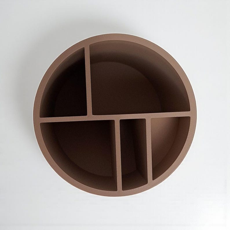 May include: A brown, circular wall shelf with five compartments. The shelf is made of a solid material and is mounted on a white wall. The compartments are of varying sizes, providing storage for small items.