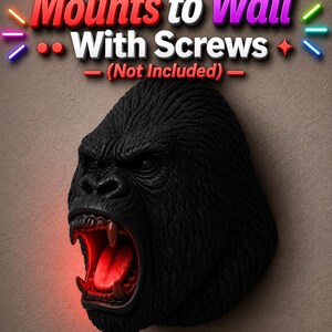 May include: A black gorilla head sculpture with an open mouth revealing red lighting. The sculpture has detailed fur texture and is designed to mount to a wall. The text "Mounts to Wall With Screws (Not Included)" is above the sculpture.