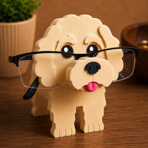 May include: A beige dog-shaped eyeglasses holder with black-framed glasses. The dog has black eyes, a black nose, and a pink tongue. The holder is made of a textured material and is designed to hold eyeglasses.