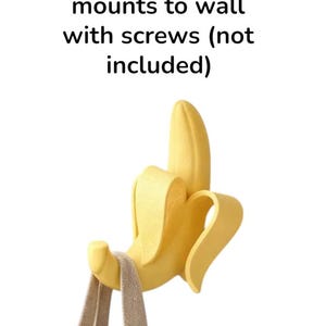 May include: A yellow banana-shaped wall hook with a tan strap hanging from it. The hook is designed to mount to a wall with screws, as indicated by the text "mounts to wall with screws (not included)".