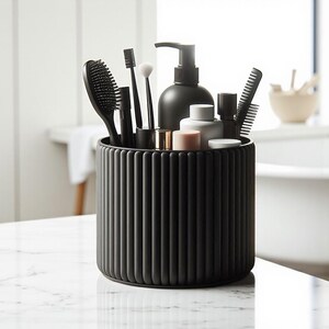 May include: A black, ribbed cylindrical organizer on a marble surface, holding various black bathroom accessories. Items include a hairbrush, toothbrush, makeup brushes, comb, and a soap dispenser. The organizer is filled with toiletries and grooming tools.