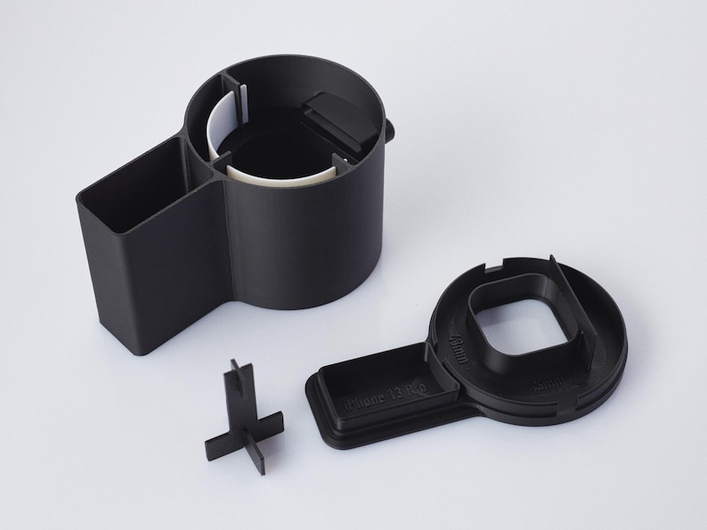 Op de afbeelding: Zwarte plastic auto-organizer met een bekerhouder, een klein vak en een verwijderbare telefoonhouder. De telefoonhouder heeft het label "Phone Dock".