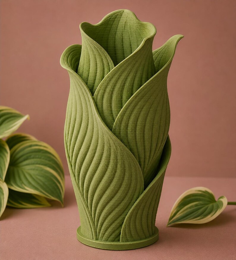 May include: A green, leaf-shaped vase with a textured surface. The vase is designed to resemble a flower bud, with overlapping leaves creating a unique and naturalistic form. The vase is approximately 10 inches tall and is suitable for displaying flowers or as a decorative piece.