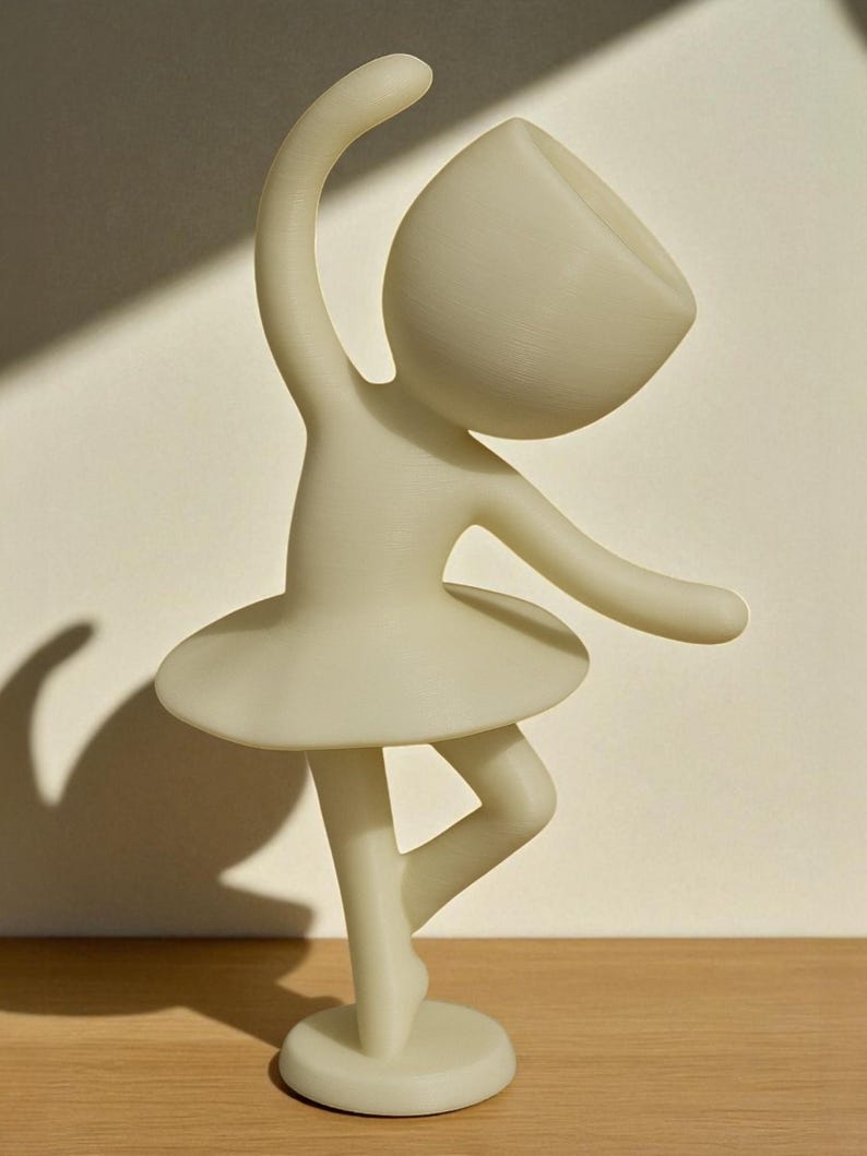 May include: A cream-colored figurine of a ballerina in a graceful pose. The figure has a rounded head, outstretched arms, and a tutu. The ballerina is balanced on one leg, with the other bent. The figurine is on a round base.