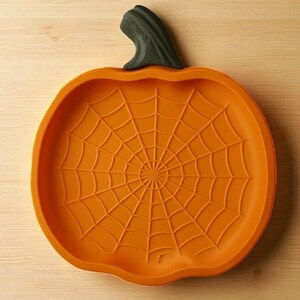 May include: Orange pumpkin-shaped serving dish with a spiderweb design. The dish has a dark green stem and is made of a durable material. Perfect for Halloween or fall-themed gatherings. The dish is approximately 10 inches in diameter.