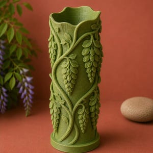 Puede incluir: Un jarr&oacute;n cil&iacute;ndrico verde con una superficie texturizada y un borde superior ondulado. El jarr&oacute;n est&aacute; adornado con un relieve detallado de vides de glicina y racimos de flores colgantes. El jarr&oacute;n mide unos 20 cm de alto.