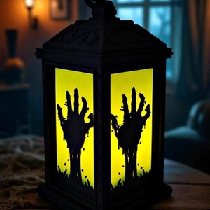 May include: Black Halloween lantern with a yellow interior, featuring silhouettes of zombie hands reaching upwards. The lantern is made of dark material and sits on a wooden surface, creating a spooky ambiance.