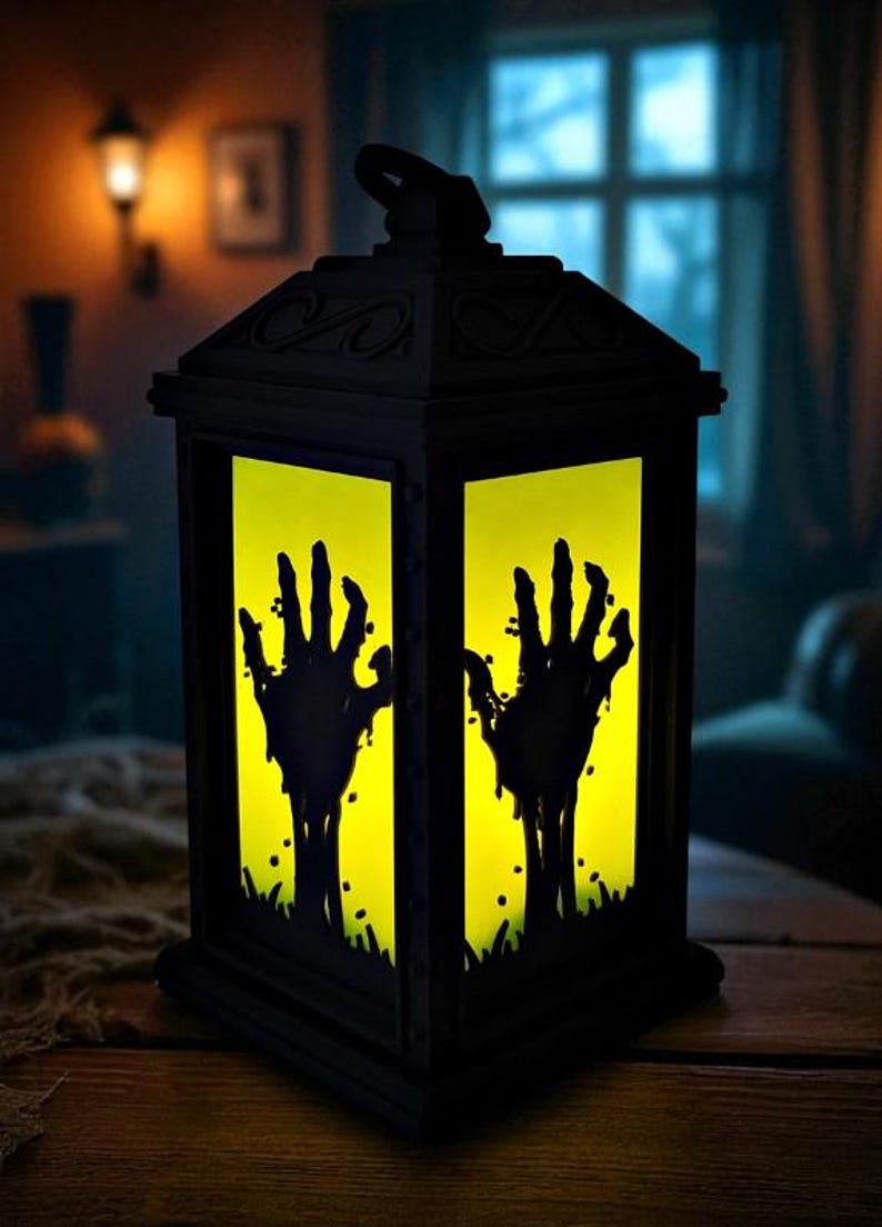 May include: Black Halloween lantern with a yellow interior, featuring silhouettes of zombie hands reaching upwards. The lantern is made of dark material and sits on a wooden surface, creating a spooky ambiance.