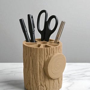 May include: A beige desk organizer shaped like a tree stump, holding black pens, a pair of scissors, and a silver pen. The organizer has a textured surface and a circular accent on the side, providing a rustic aesthetic.