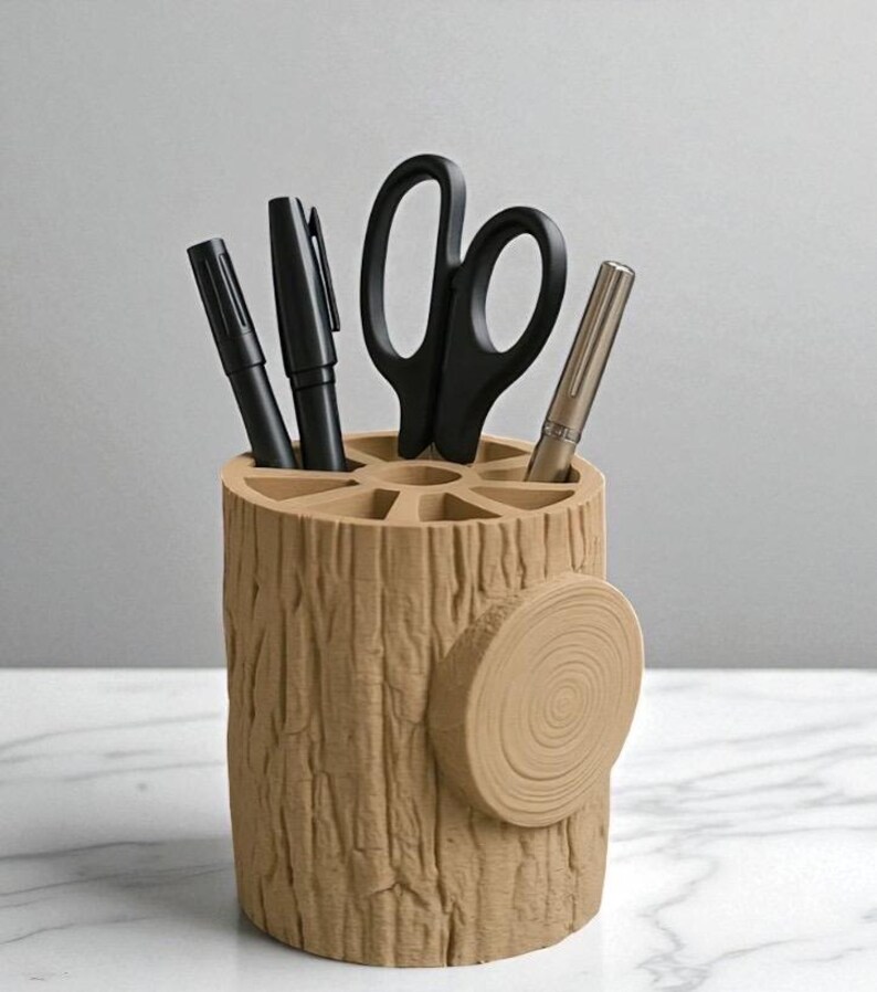 May include: A beige desk organizer shaped like a tree stump, holding black pens, a pair of scissors, and a silver pen. The organizer has a textured surface and a circular accent on the side, providing a rustic aesthetic.