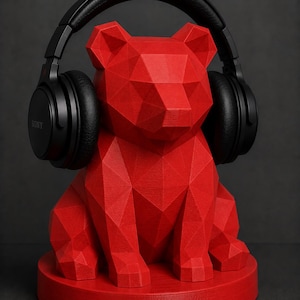 Puede incluir: Un soporte para auriculares con forma de oso geom&eacute;trico rojo con auriculares negros encima. El soporte est&aacute; hecho de una serie de formas triangulares y se asienta sobre una base circular. Los auriculares tienen la marca "SONY".
