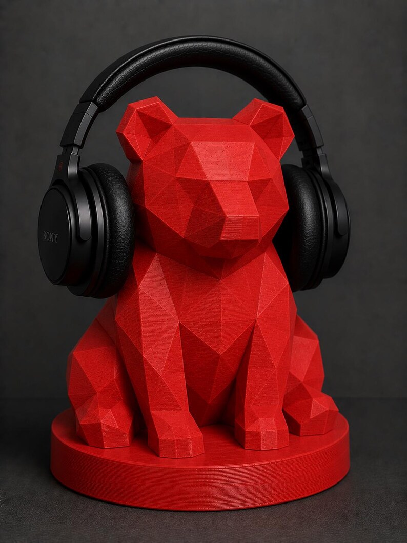 Puede incluir: Un soporte para auriculares con forma de oso geom&eacute;trico rojo con auriculares negros encima. El soporte est&aacute; hecho de una serie de formas triangulares y se asienta sobre una base circular. Los auriculares tienen la marca "SONY".