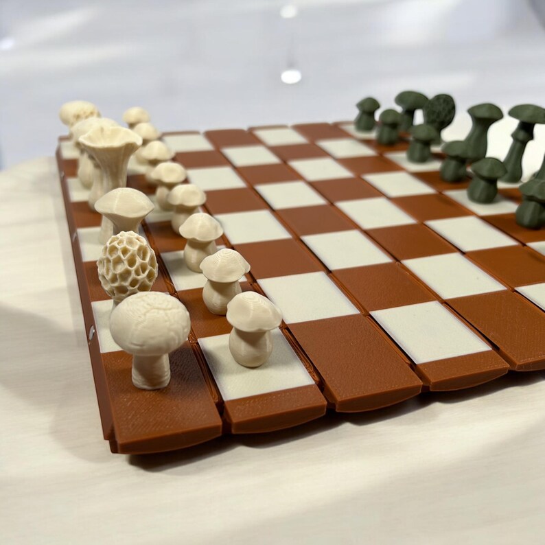 May include: A novelty chess set with mushroom-shaped pieces in cream and green. The board has a brown and white chequered pattern. The pieces are detailed, with different mushroom types. A creative and whimsical board game, perfect for a gift.