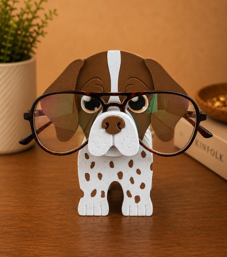 May include: A whimsical dog-shaped eyeglass holder. The holder is white with brown spots and a brown and white head. It is holding a pair of brown-rimmed eyeglasses. The holder is made of wood and is a decorative item.