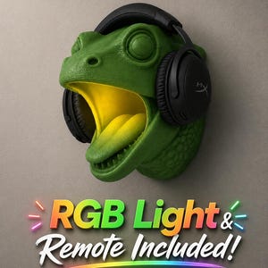 Op de afbeelding: Een groene dinosaurushoofd wandhouder met een gele binnenkant en een zwarte headset. De tekst "RGB Light & Remote Included!" wordt weergegeven in kleurrijke neonletters.