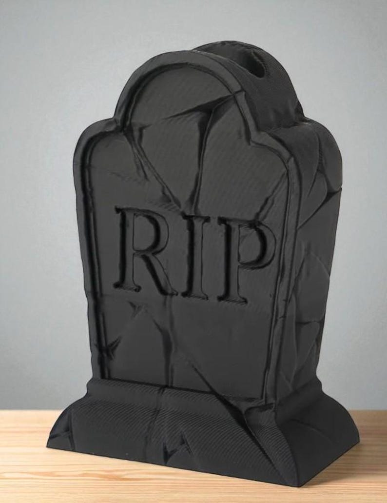May include: A black tombstone with the letters "RIP" carved into the front. The tombstone has a textured surface and a rounded top. The base is rectangular. The tombstone is a Halloween decoration.