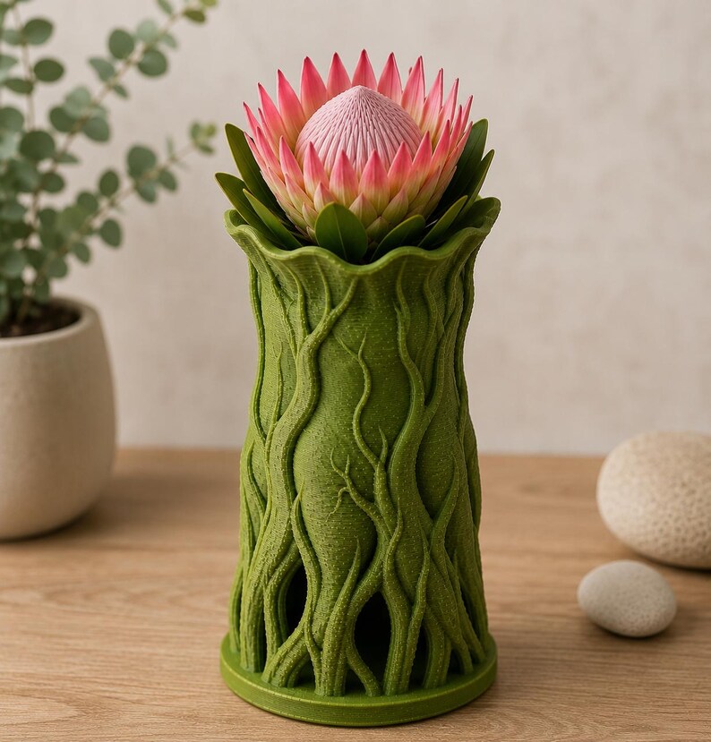 May include: A green vase with a textured, tree-like design, holding a pink and green protea flower. The vase has a wide base and a flared top. The flower has a central, textured pink bloom surrounded by pink petals and green leaves.
