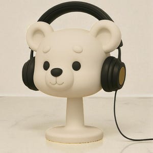 May include: A white bear-shaped decorative object with black headphones. The bear has black eyes and a black nose. The headphones have black earcups with gold accents and a black headband. A black cord extends from the headphones.