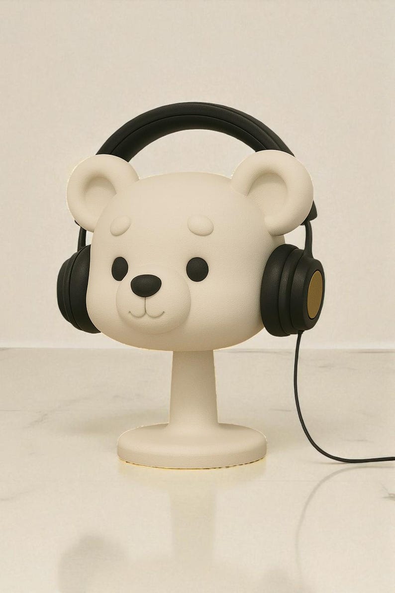 May include: A white bear-shaped decorative object with black headphones. The bear has black eyes and a black nose. The headphones have black earcups with gold accents and a black headband. A black cord extends from the headphones.