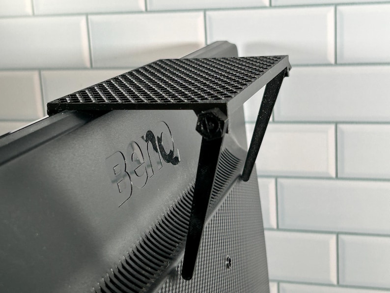 May include: Black monitor stand with a grid pattern on the top shelf. The stand is attached to the back of a black monitor with the BenQ logo visible.