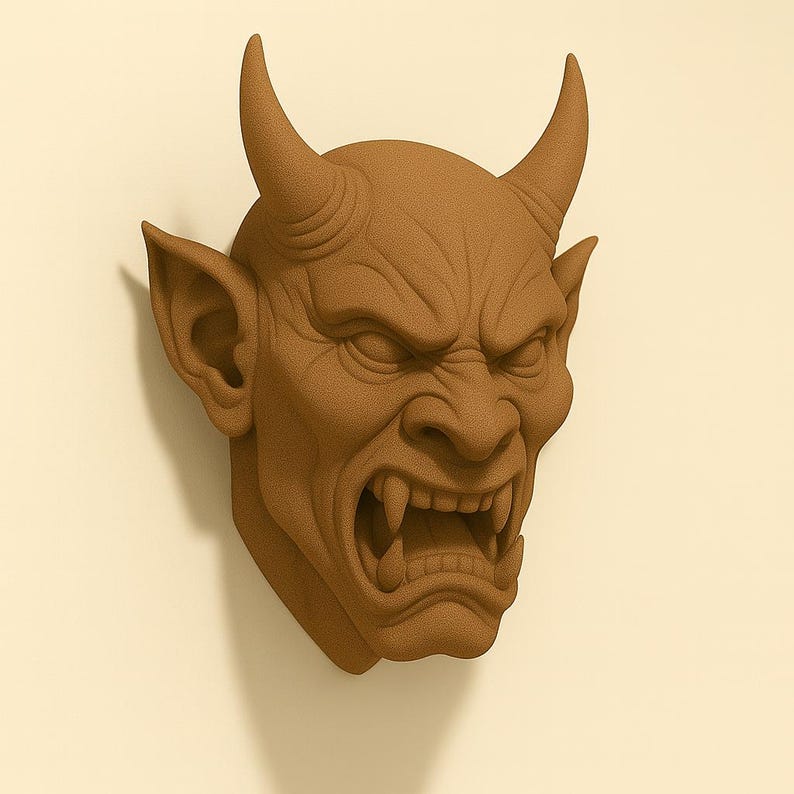 May include: A brown, textured wall sculpture of a demonic face with horns, pointed ears, and an open mouth revealing sharp teeth. The sculpture is mounted on a light beige wall, creating a striking contrast.